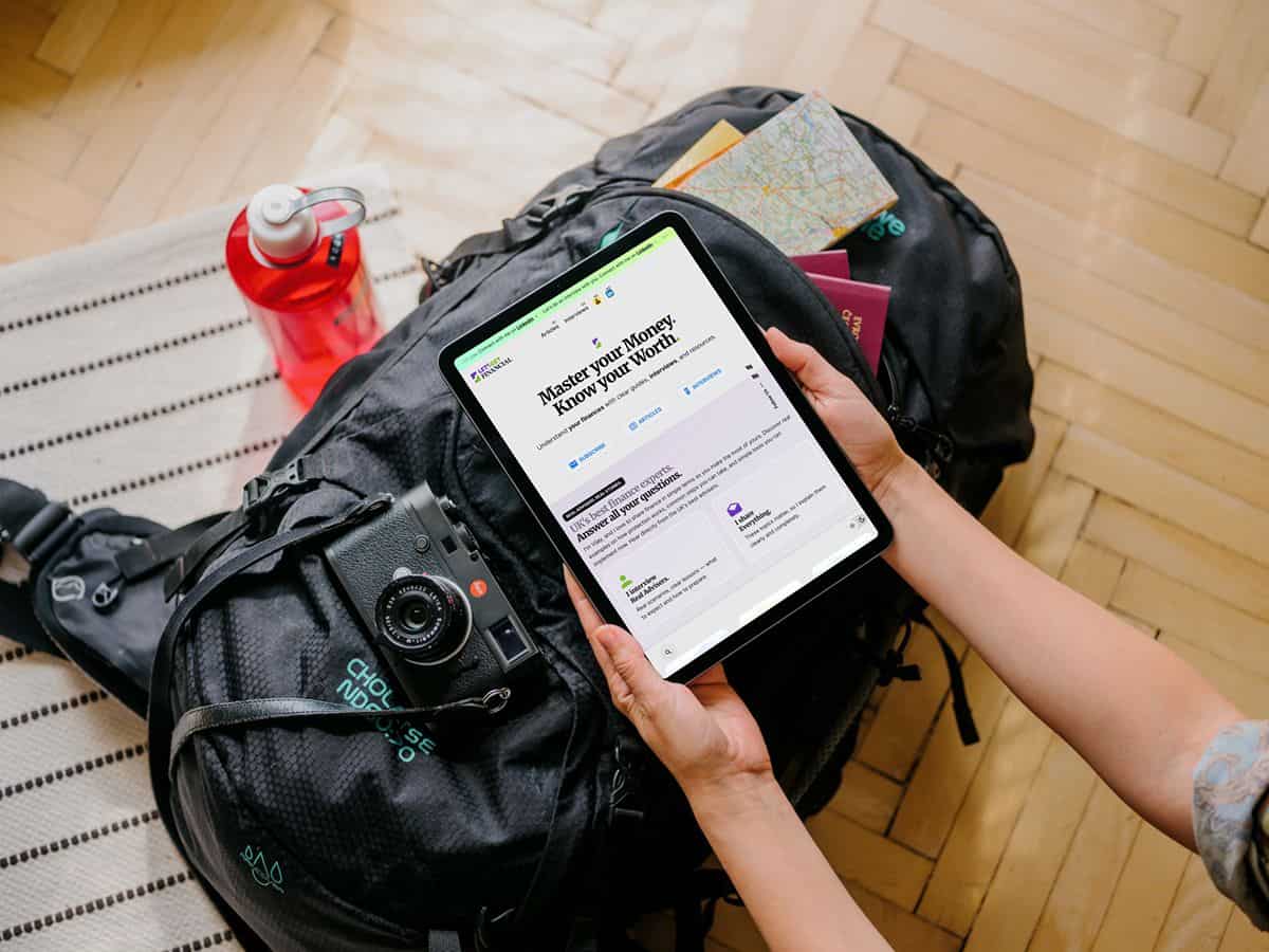 Person using tablet browsing financial education website whilst packing for travel
